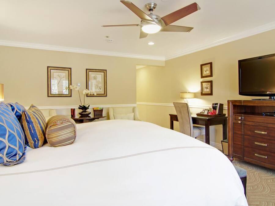 A hotel room with a large bed, a desk with a chair, a television, and a ceiling fan.