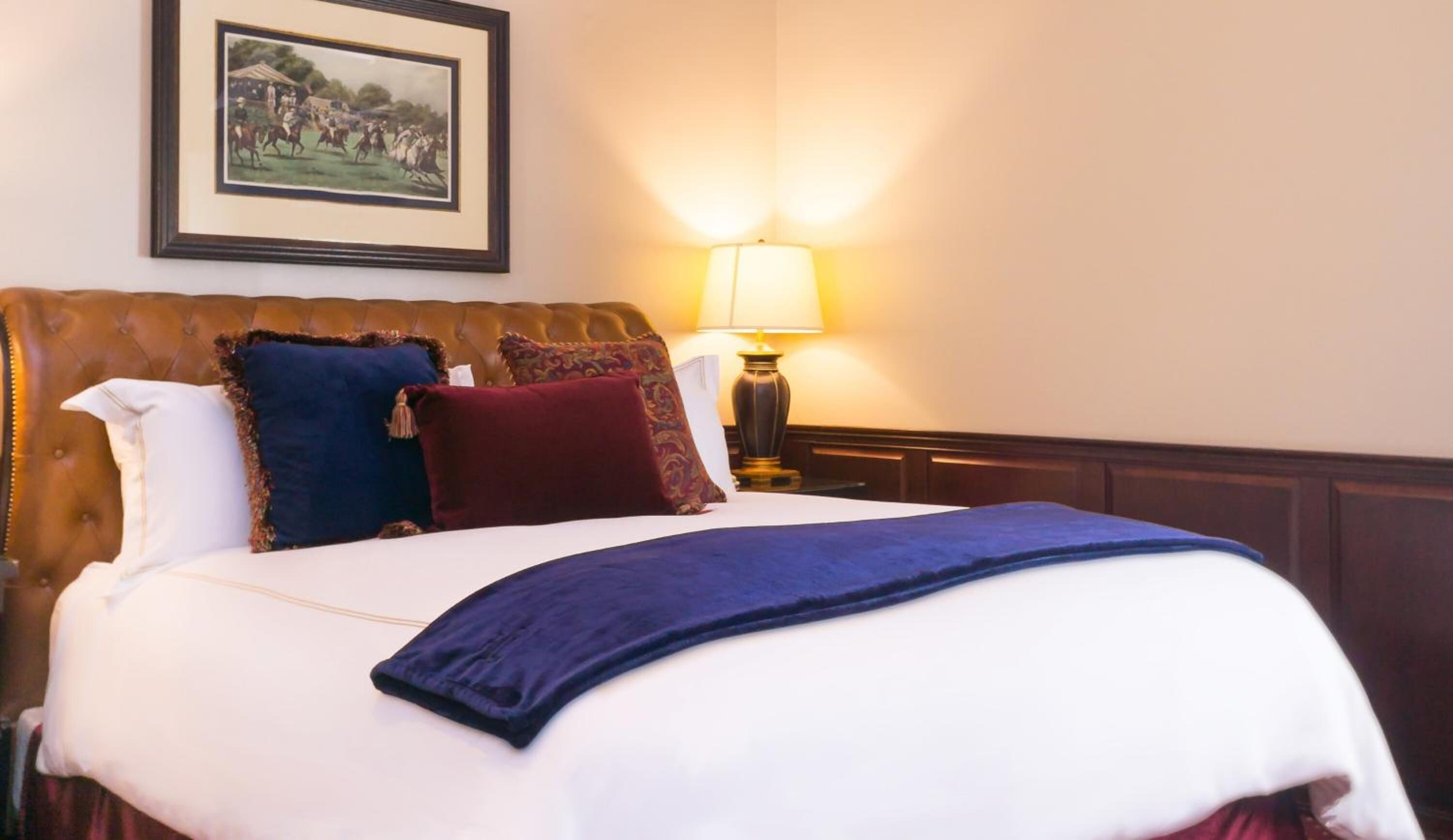 A neatly made bed with a blue blanket, a brown headboard, and several decorative pillows.
