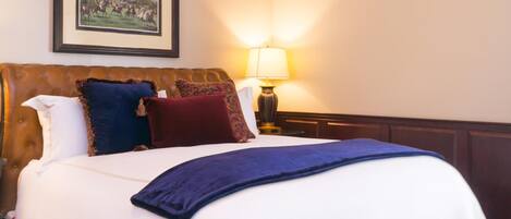 A neatly made bed with a blue blanket, a brown headboard, and several decorative pillows.