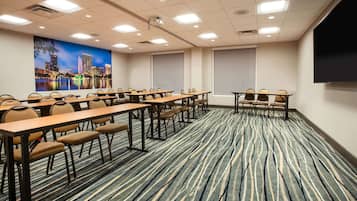 Sala de conferências com um mural da paisagem urbana, várias mesas com cadeiras e uma tela grande.