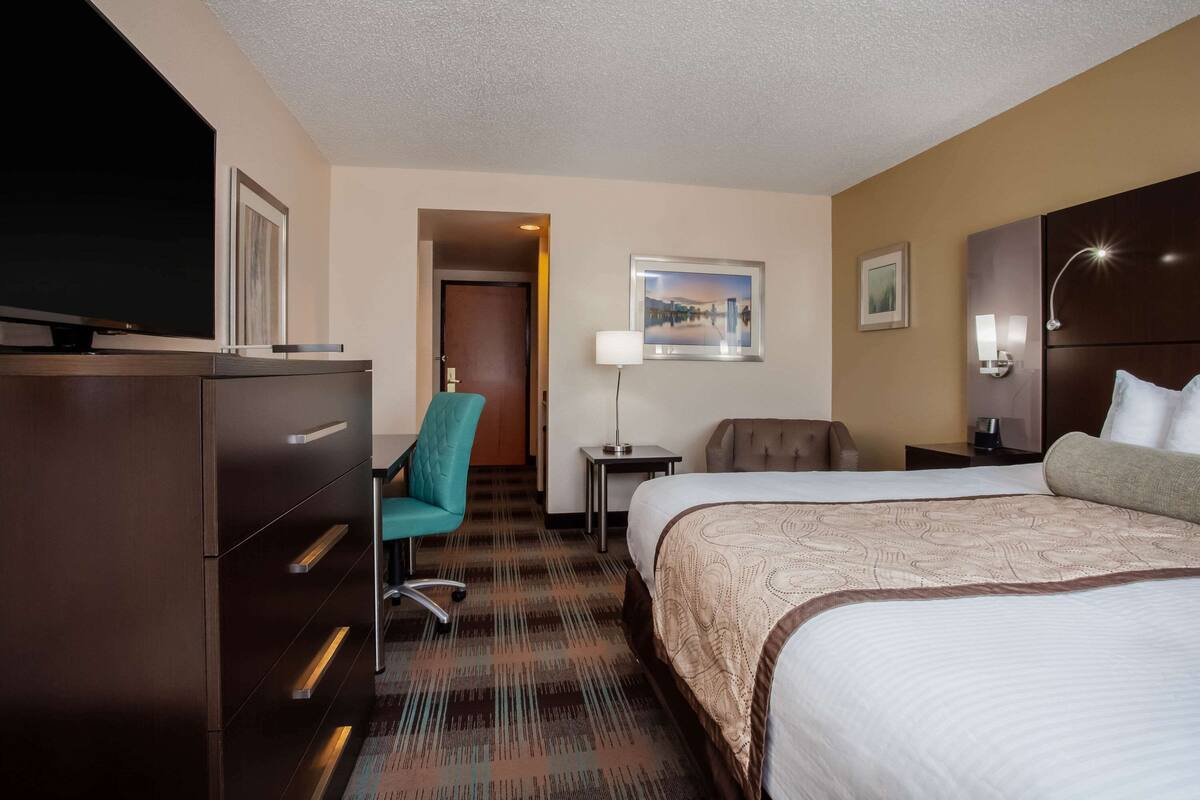 A hotel room with a large bed, a desk with a lamp, a chair, and a TV on a dresser.