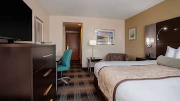 Une chambre d’hôtel avec un grand lit, un bureau avec une lampe, une chaise et un téléviseur posé sur une commode.