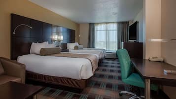 A hotel room with two beds, a desk, a chair, a TV, and a window with curtains.