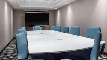 Un salón de conferencias con una gran mesa y sillas azules, un televisor de pantalla plana y piso alfombrado.
