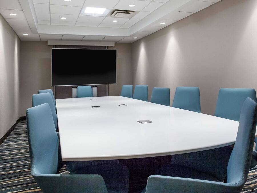 A conference room with a large table and blue chairs, a flat-screen TV, and a carpeted floor.