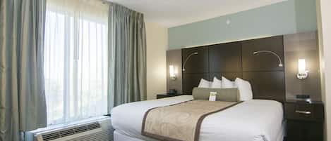 Camera d'albergo con un letto grande, un comodino, una lampada a parete e una finestra con tende.