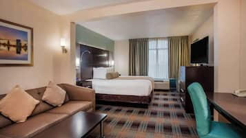 A hotel room with a bed, a sofa, a desk, a TV, and a painting on the wall.