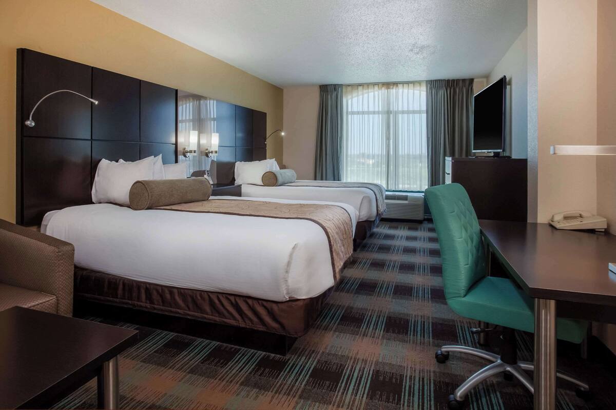 A hotel room with a large bed, a desk, a chair, a TV, and a phone.