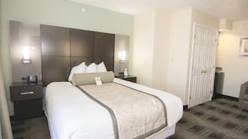 Quarto de hotel com uma cama grande, duas mesas de cabeceira, um criado-mudo, uma luminária, uma luz na parede e uma porta.