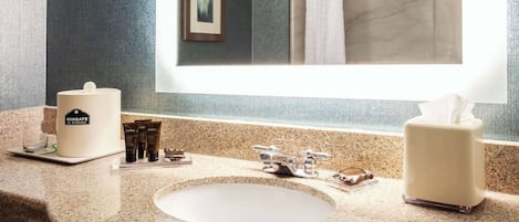 A bathroom with a granite countertop, a sink, a mirror, a framed picture, and a shower curtain.