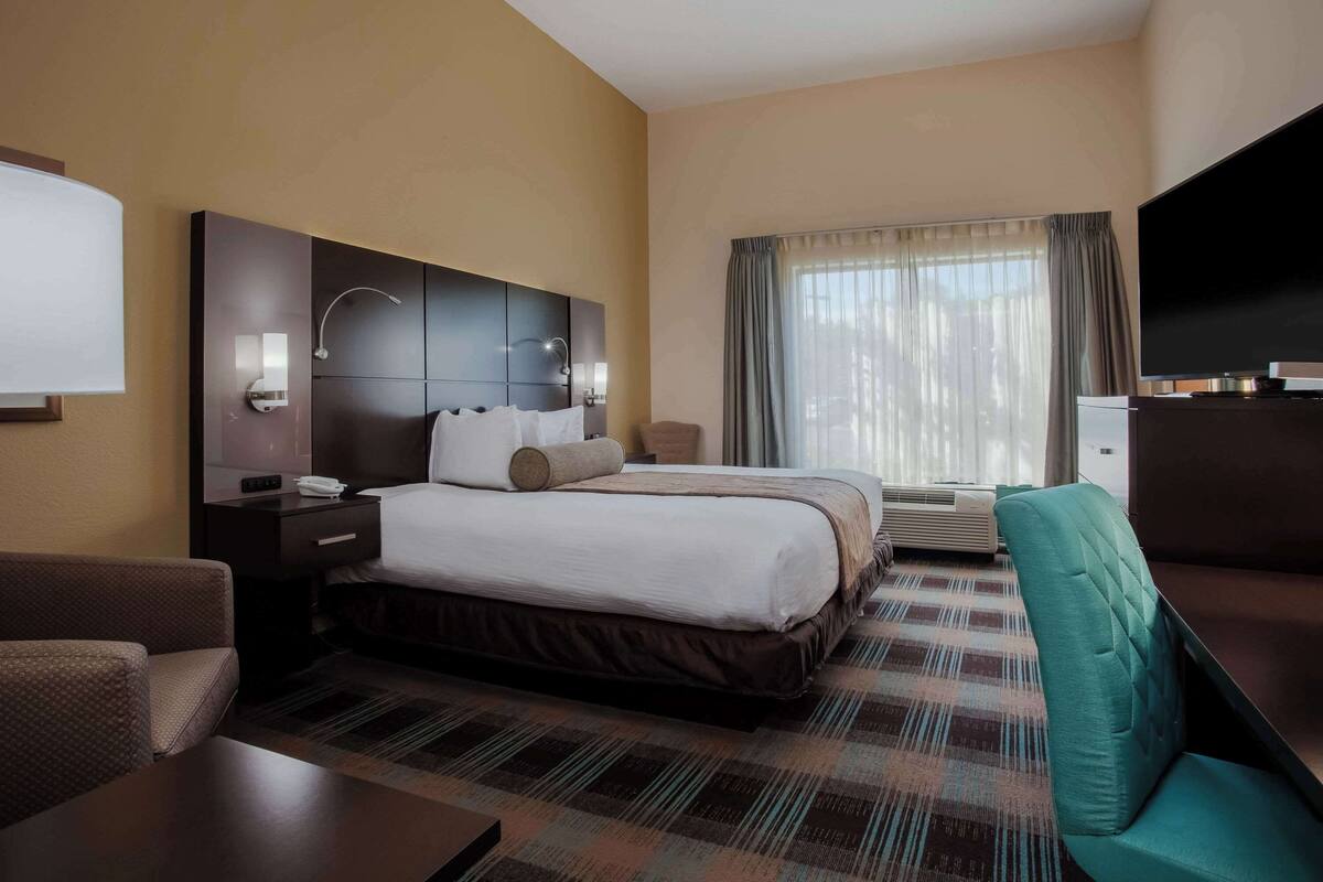 A hotel room with a large bed, a desk, a chair, a TV, and a window with curtains.