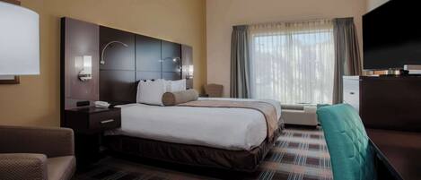 Habitación de hotel con una cama grande, un escritorio, una silla, un televisor y una ventana con cortinas.