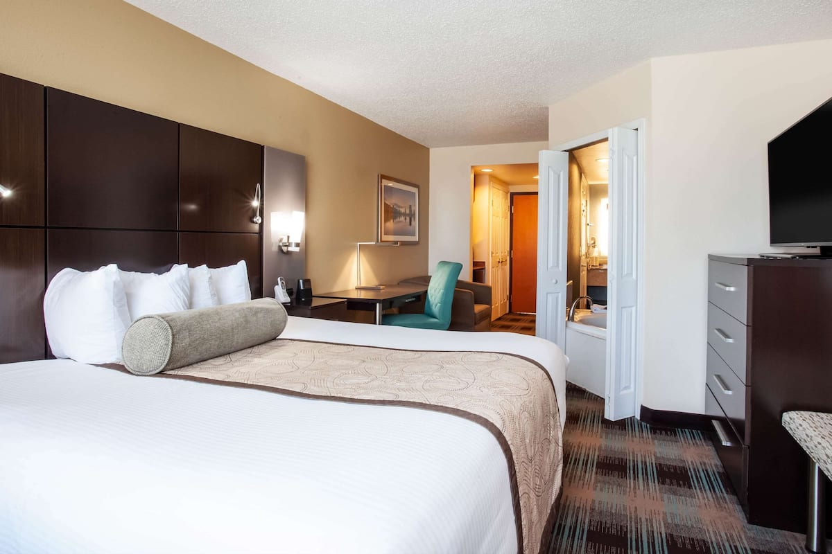 A hotel room with a large bed, a desk, a chair, a television, and a wardrobe.