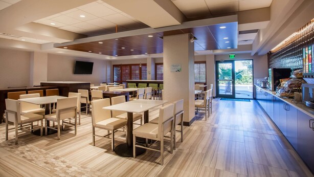 A modern restaurant with multiple dining tables and chairs, a bar area, and a television mounted on the wall. - Wingate by Wyndham - Orlando International Airport (Orlando)