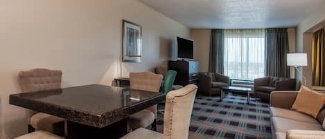 A hotel room with a dining table, chairs, a sofa, a TV, and a patterned carpet.