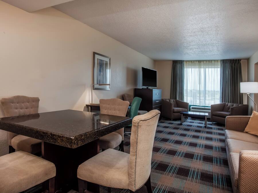 Habitación de hotel con una mesa de comedor, sillas, un sofá, un televisor y una alfombra estampada.