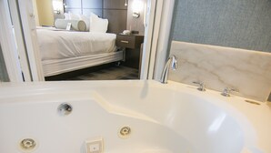 A modern hotel room with a large white bathtub, a neatly made bed, and a small bedside table with a lamp. - Wingate by Wyndham - Orlando International Airport (Orlando)