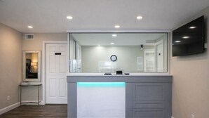 A reception desk with a mirror, a clock, and a flat-screen TV. -  Quarters Inn and Suites (Antioch)