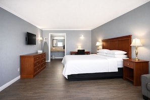 A hotel room with a bed, nightstands, a dresser, a TV, and a bathroom visible through an open door. -  Quarters Inn and Suites (Antioch)