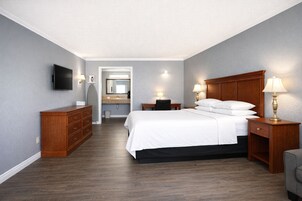 A hotel room with a bed, nightstands, a dresser, a TV, and a bathroom visible through an open door.