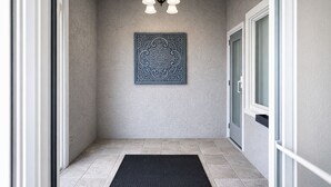 A hallway with a black doormat, a patterned wall hanging, and a ceiling light fixture. -  Quarters Inn and Suites (Antioch)