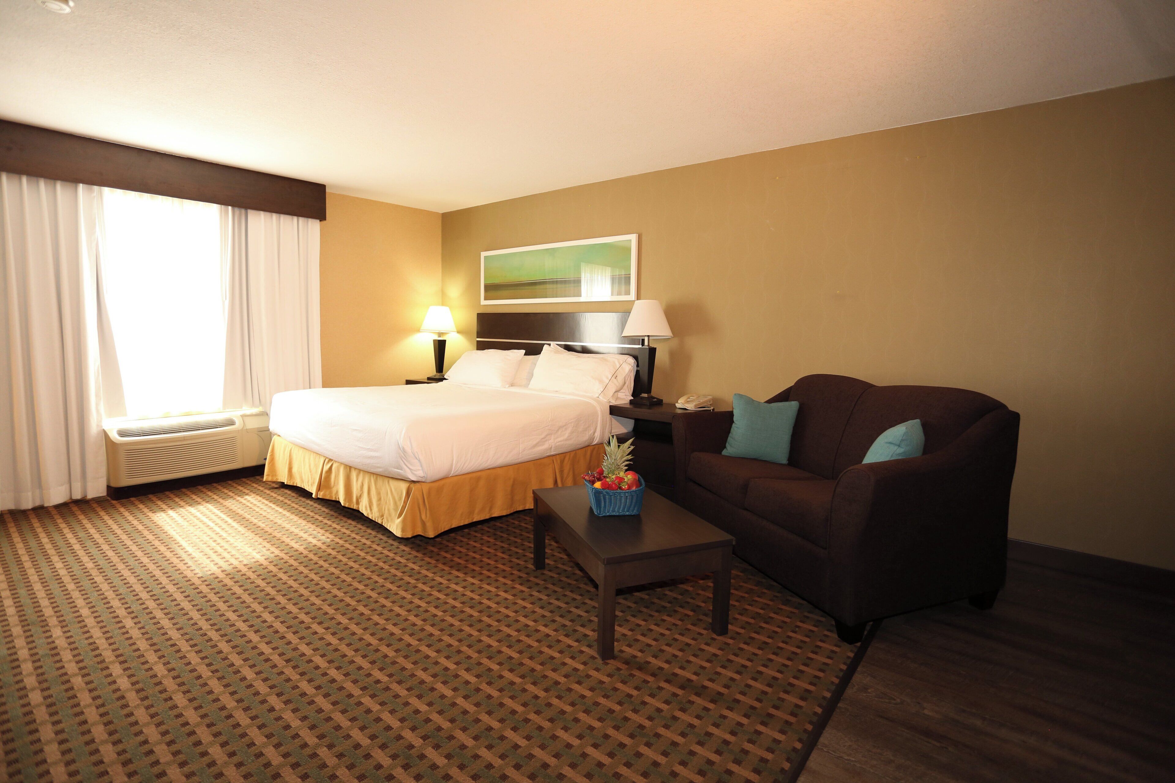 A hotel room with a bed, a desk, a chair, a window with curtains, and a painting on the wall.