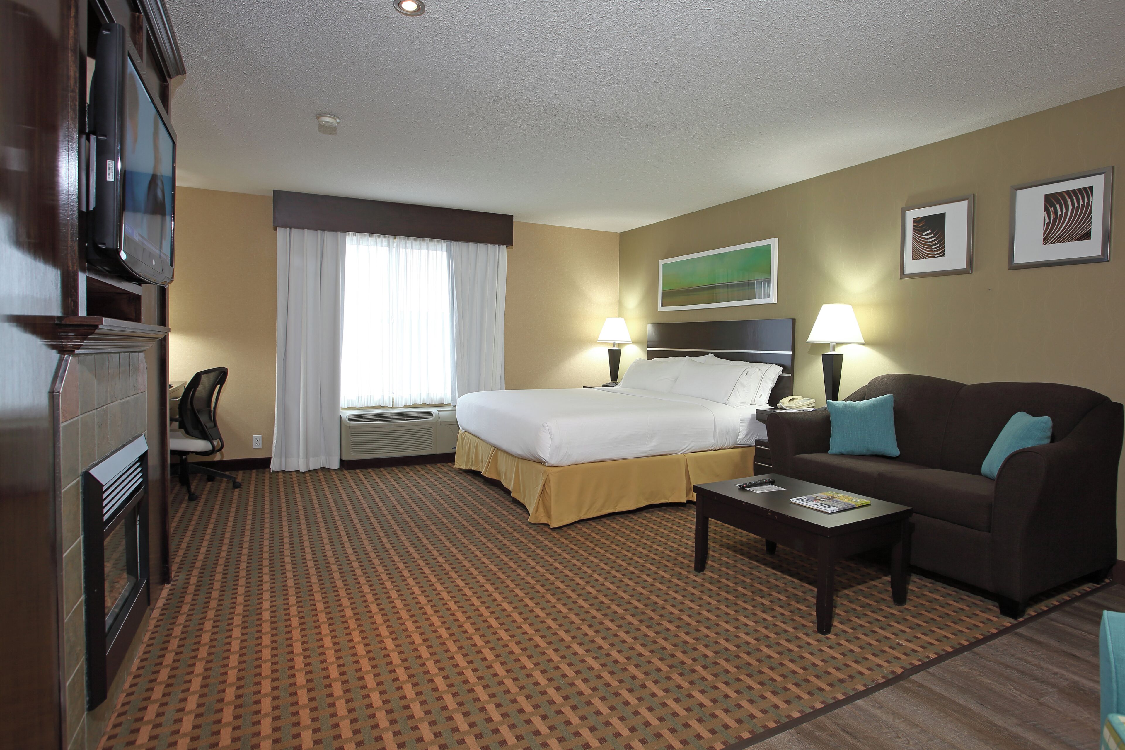 Une chambre d’hôtel avec un lit, un canapé, un bureau, une chaise, une télévision et une fenêtre avec des rideaux.