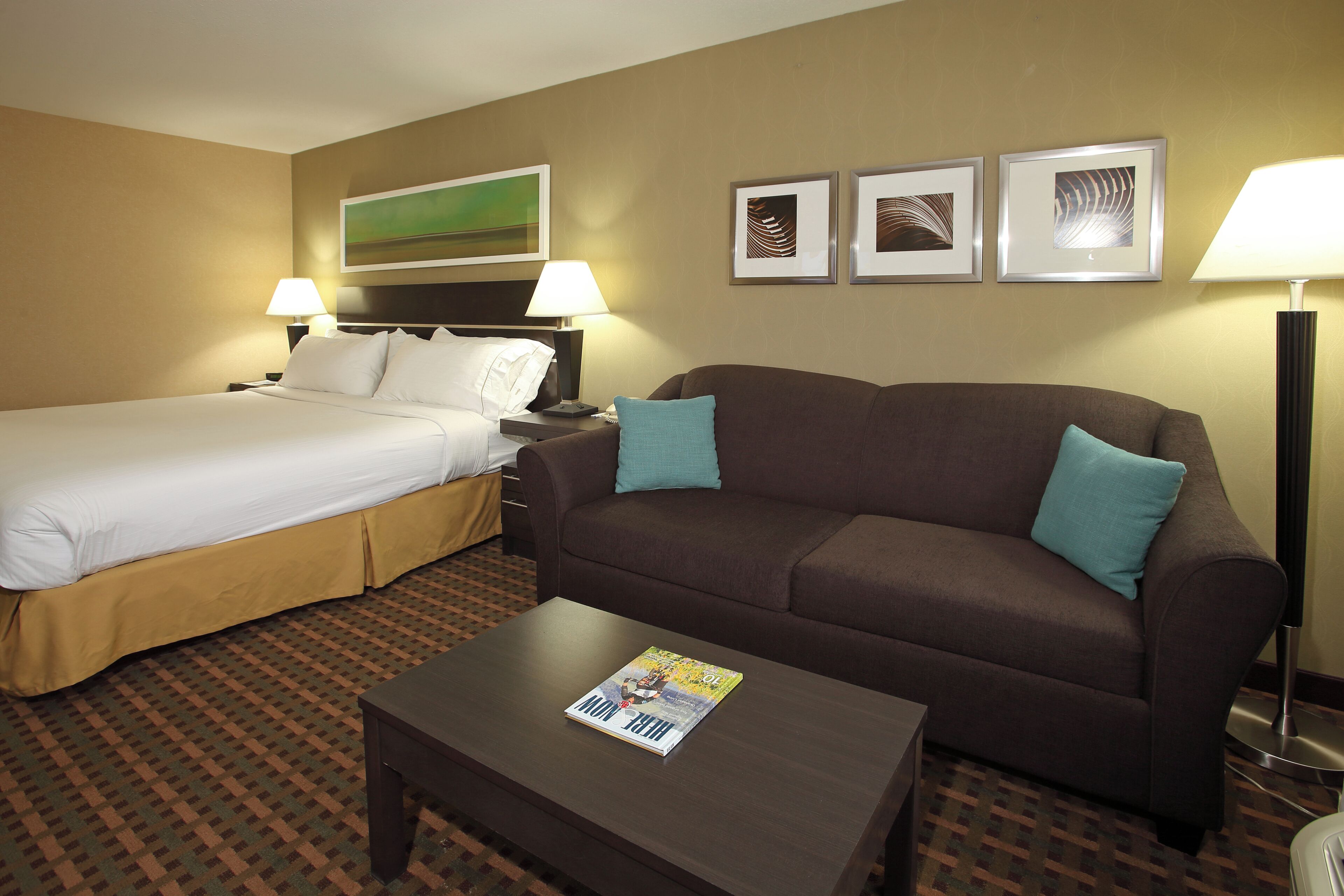 A hotel room with a bed, a sofa, a coffee table with a magazine, and a lamp.