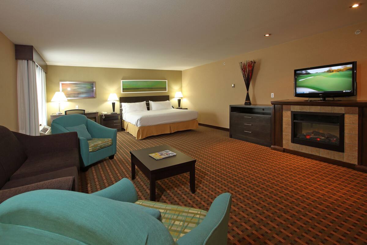 A hotel room with a bed, two armchairs, a coffee table, a TV, and a fireplace.