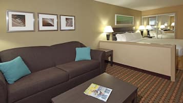 Una habitación de hotel con un sofá marrón, una mesita con una revista, una cama con ropa blanca y tres cuadros en la pared.