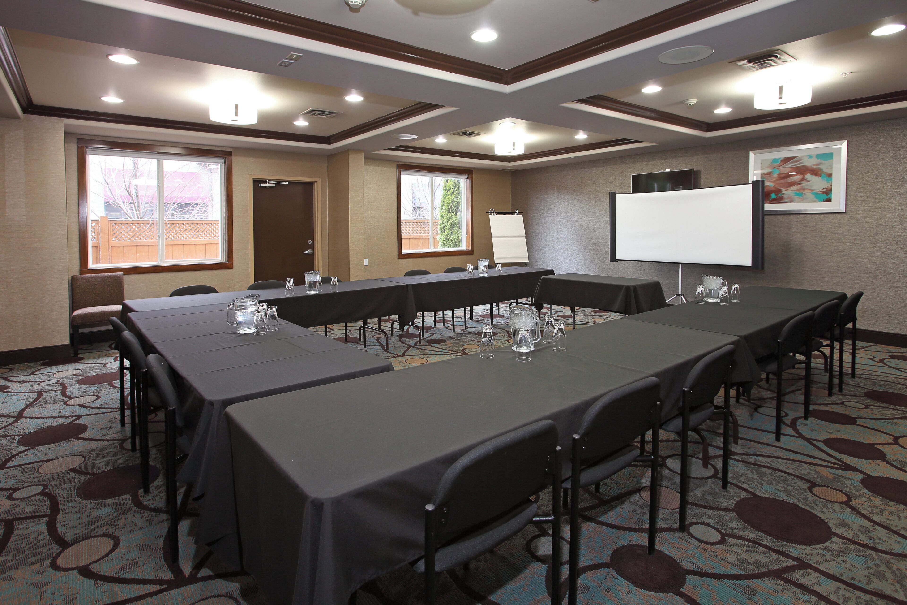 A conference room with a long table, chairs, a whiteboard, and a projector screen.