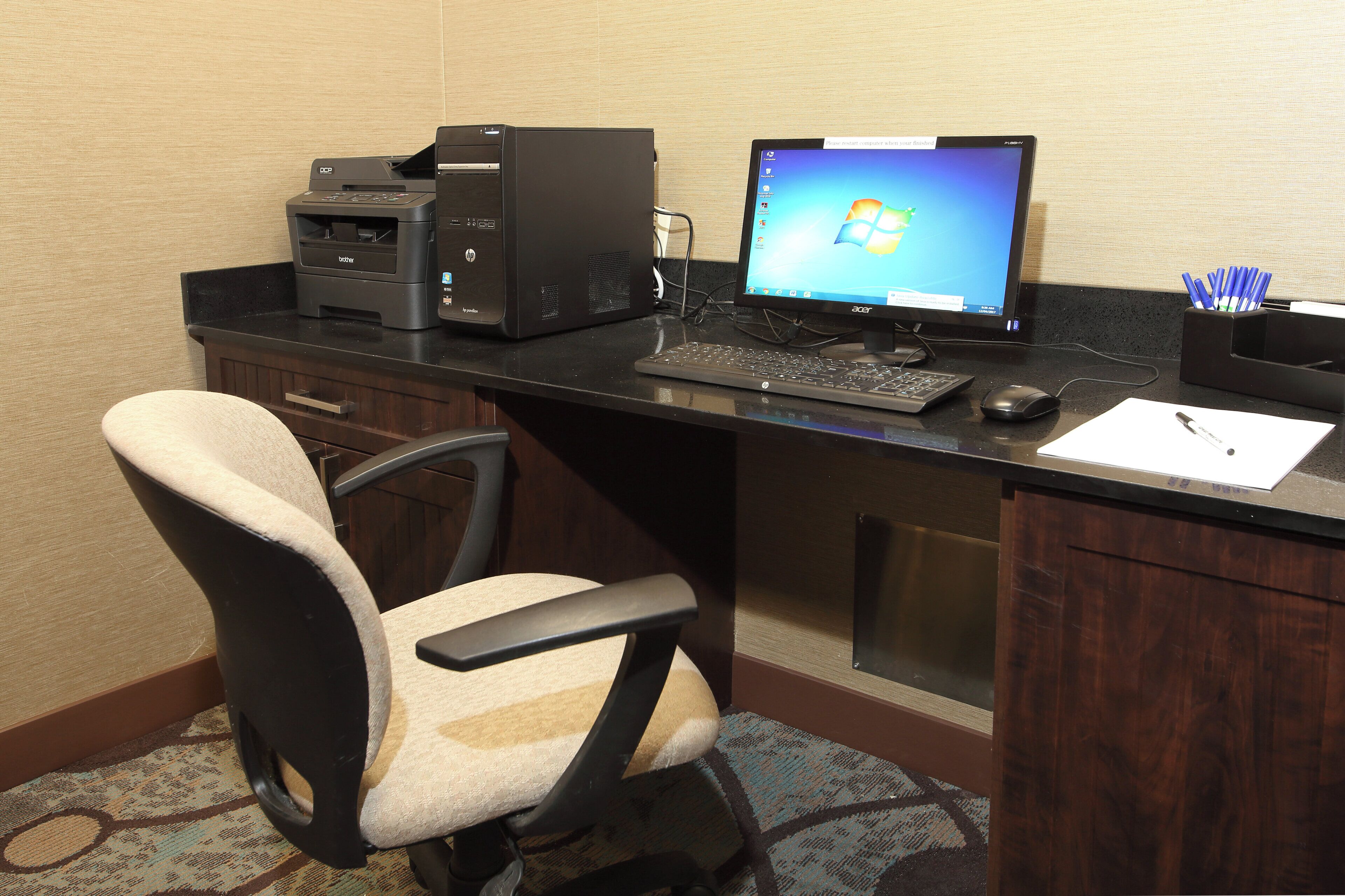 Escritorio de hotel con computadora, impresora y silla.