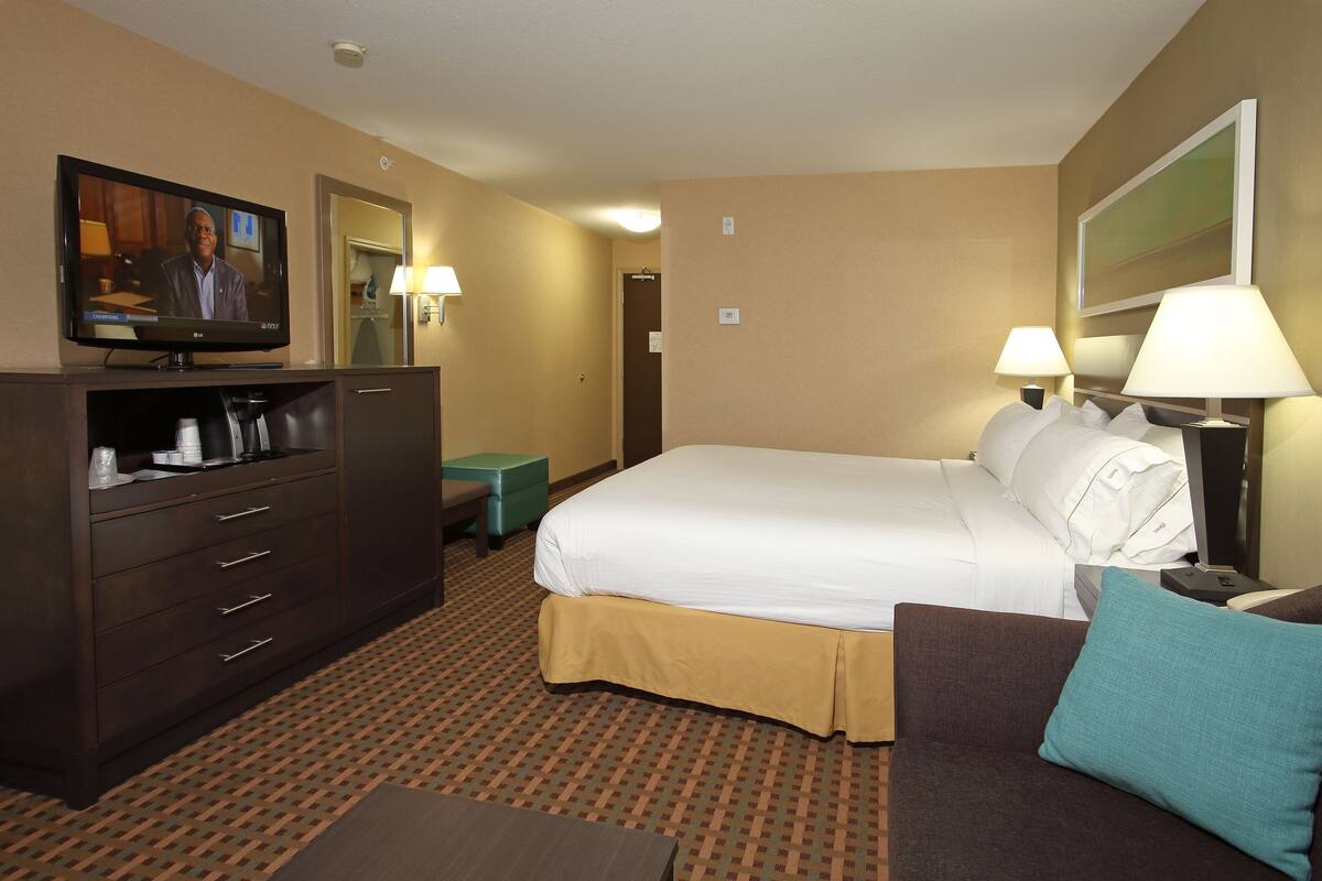 A hotel room with a bed, a TV, a desk, a chair, and a lamp.