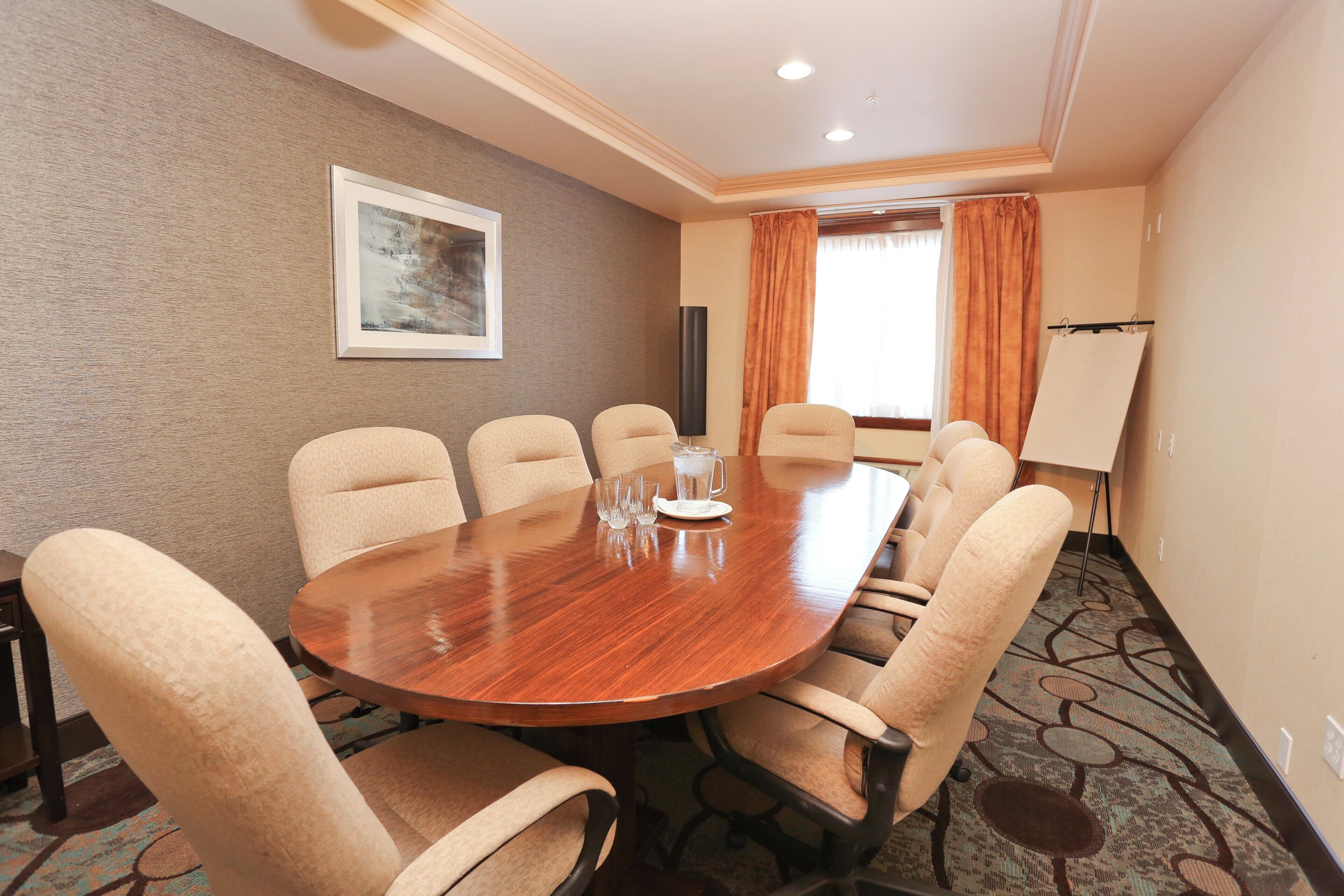 Un salón de conferencias con una mesa de madera, sillas color beige, un cuadro en la pared y una pizarra blanca a la derecha.