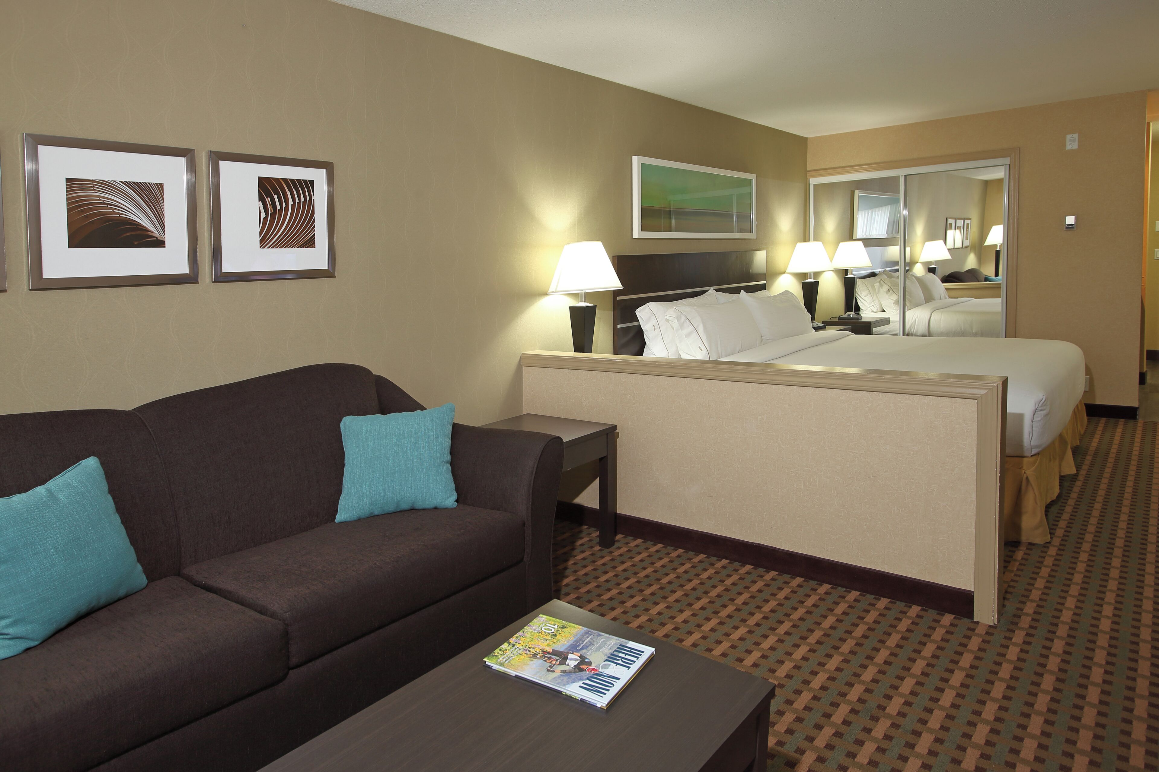 A hotel room with a sofa, a bed, a nightstand, and a magazine on the coffee table.