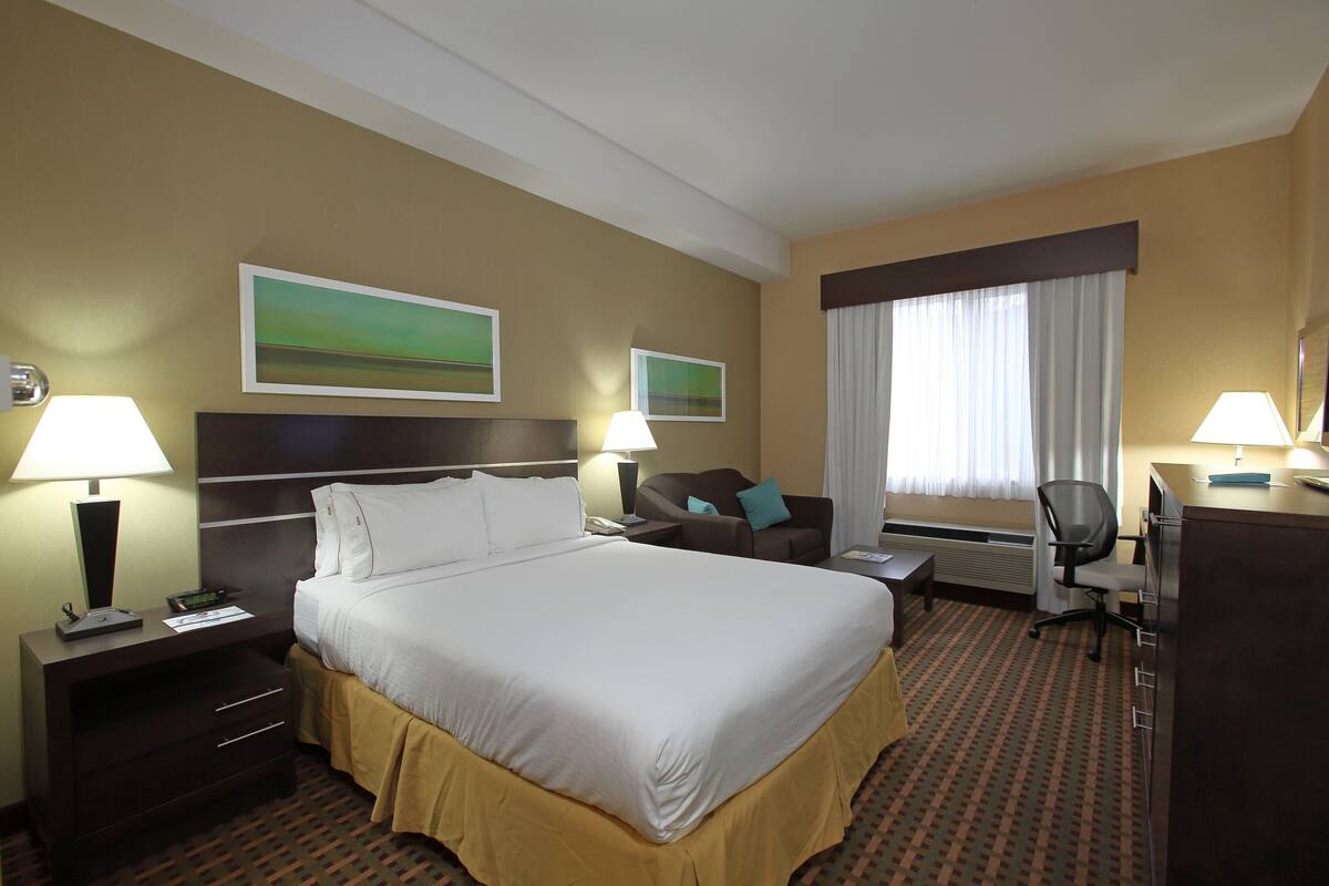 A hotel room with a large bed, a desk, a chair, a nightstand, and two wall-mounted lamps.