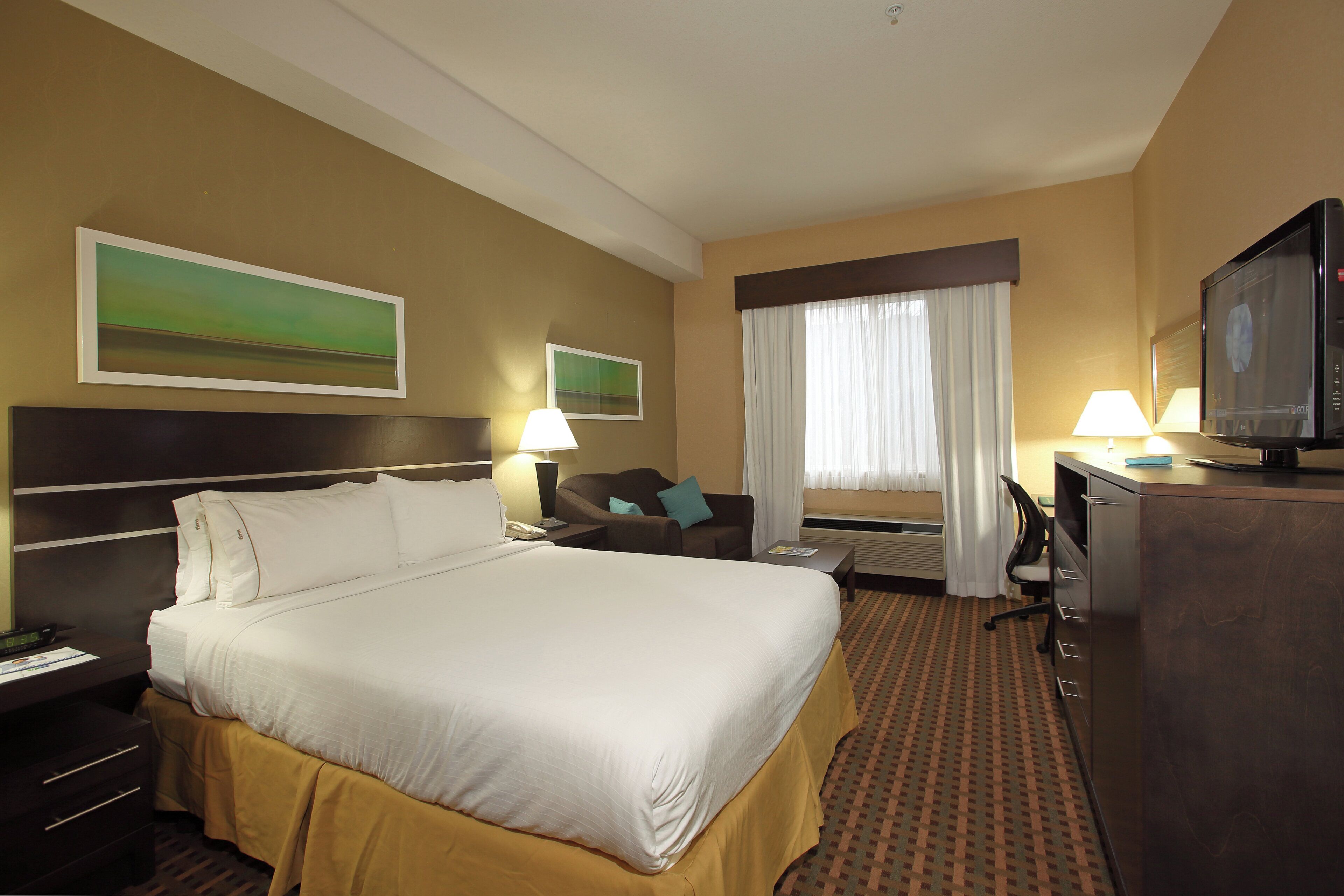 Een hotelkamer met een groot bed, een bureau, een televisie en twee schilderijen aan de muur.