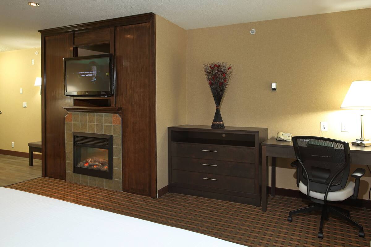 A hotel room with a fireplace, a television, a desk with a chair, and a vase with flowers.