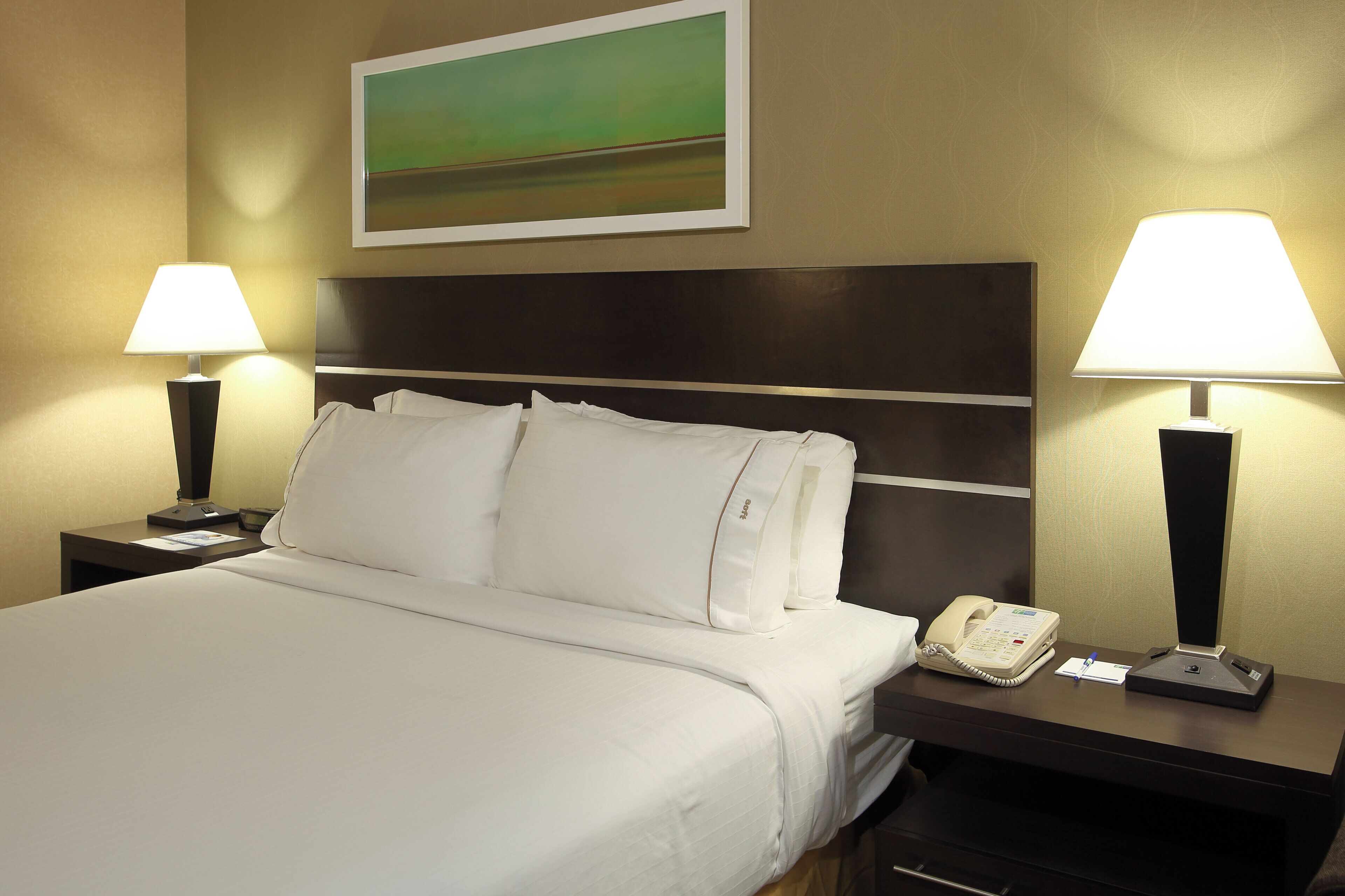 A hotel room with a large bed, two bedside tables, a nightstand with a telephone, and two wall-mounted lamps.
