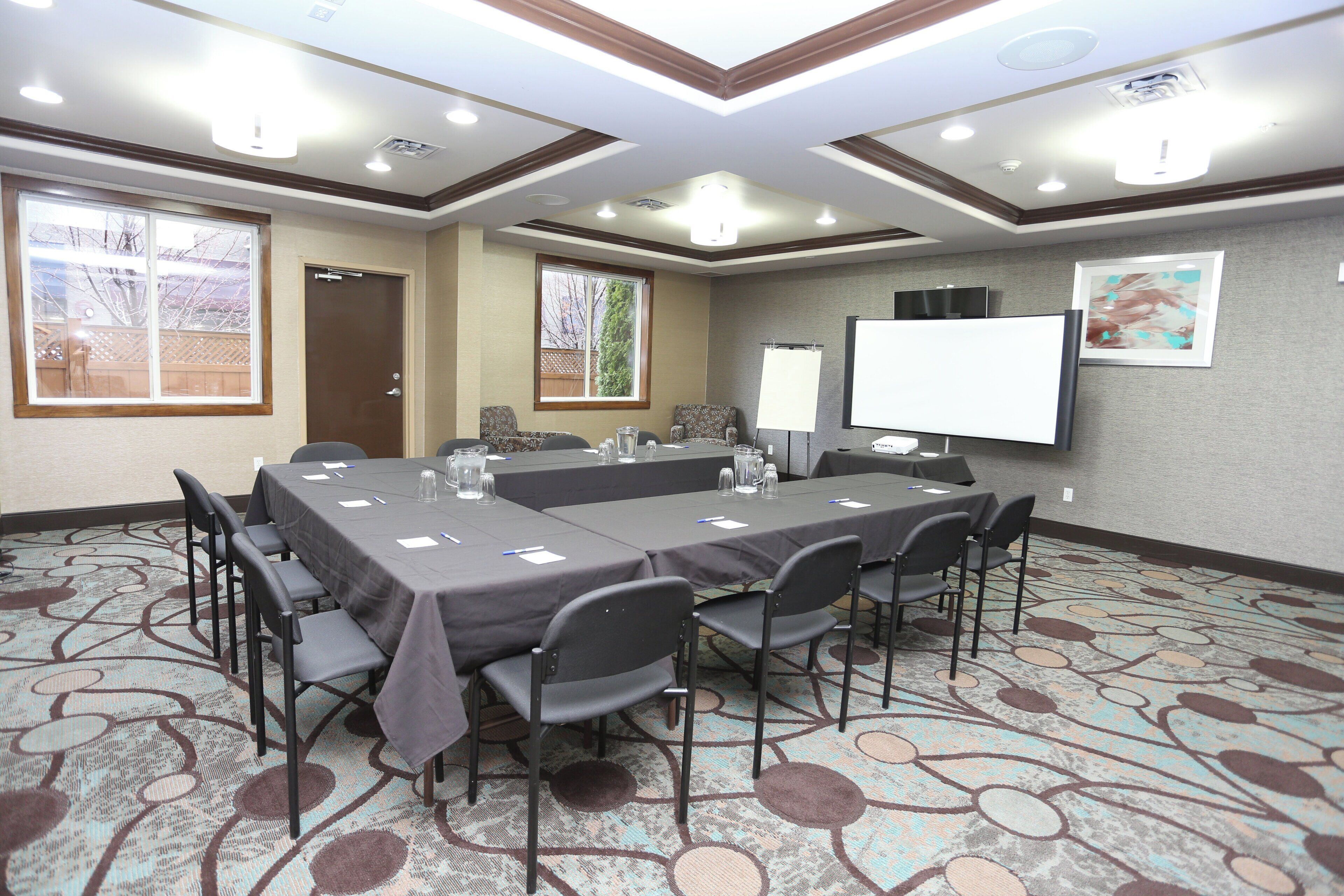 A conference room with a long table, chairs, a projector screen, and a large window.