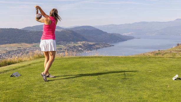 Eine Person auf einer grasbewachsenen Anhöhe mit Blick auf einen See und Berge.