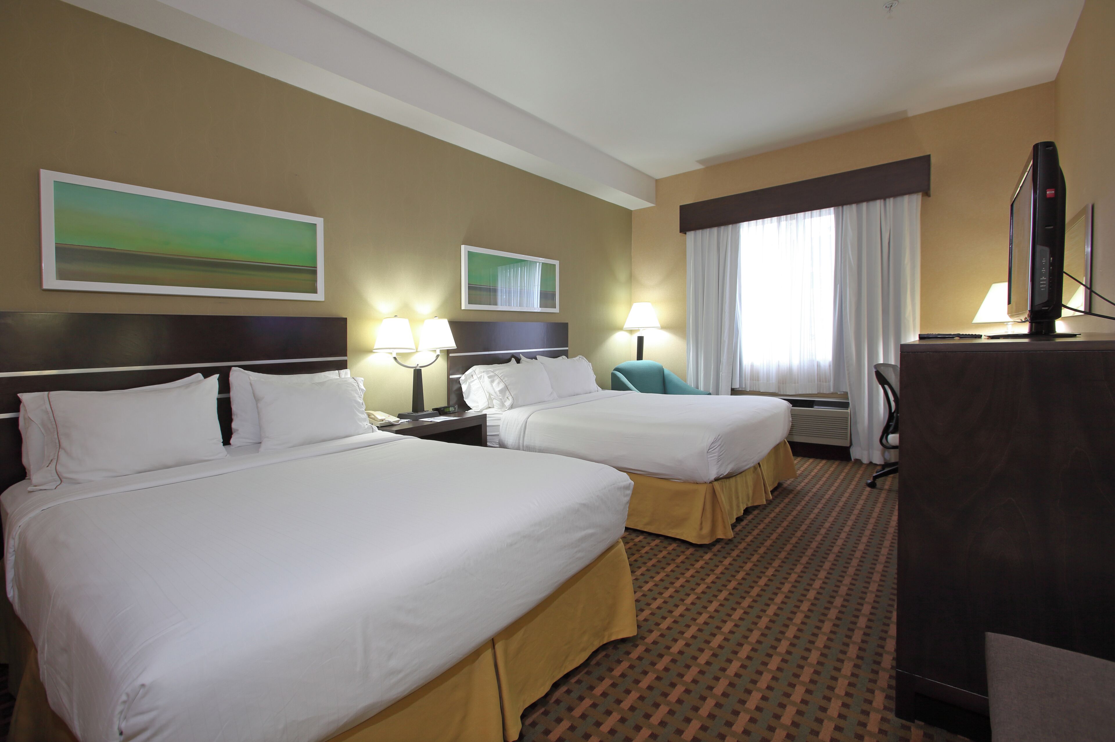 A hotel room with two beds, a desk, a TV, and a window with curtains.