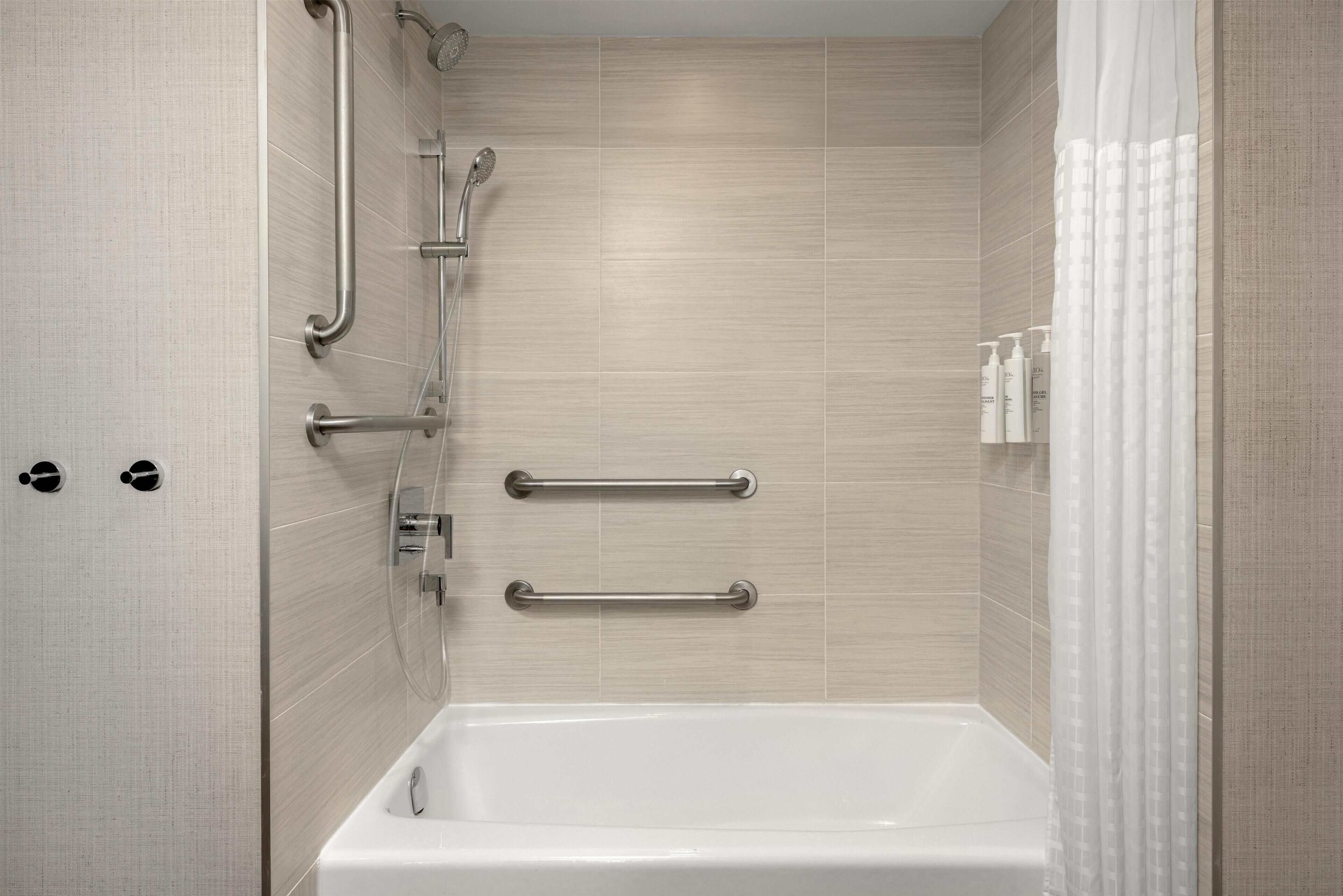 A modern bathroom with a bathtub, grab bars, and a showerhead.