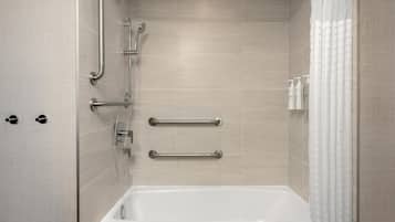 A modern bathroom with a bathtub, grab bars, and a showerhead.