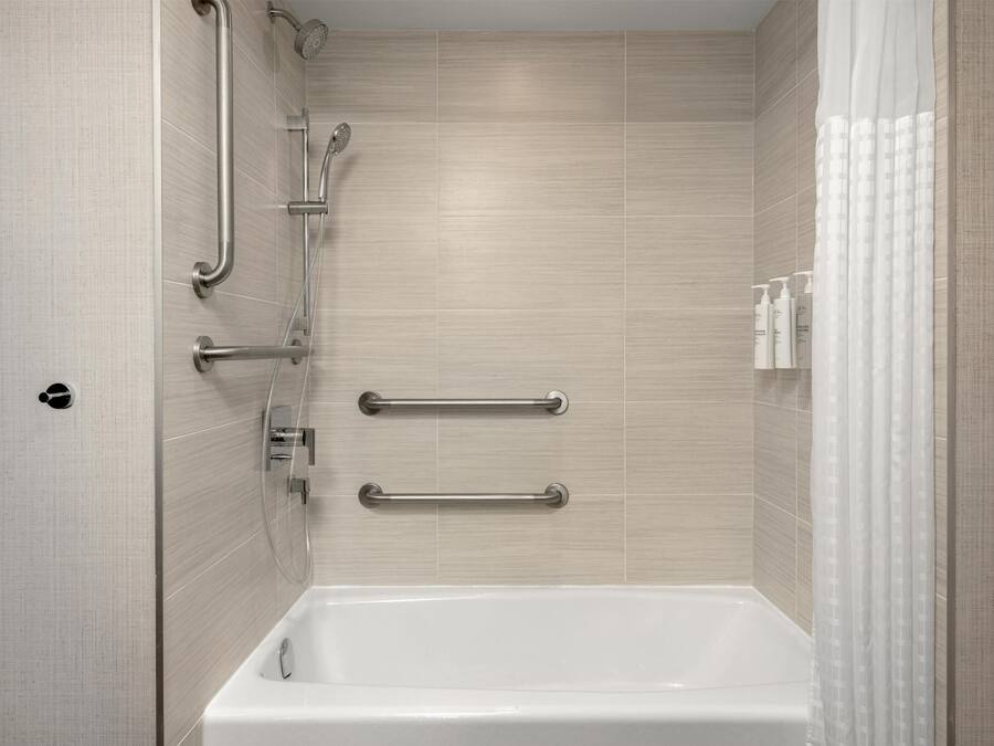 A modern bathroom with a bathtub, grab bars, and a showerhead.