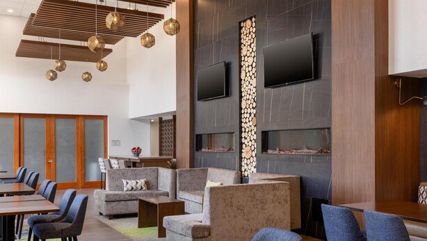 A modern hotel lobby with a wooden ceiling, round tables, sofas, and a fireplace. - Hampton Inn & Suites by Hilton Windsor (Windsor)