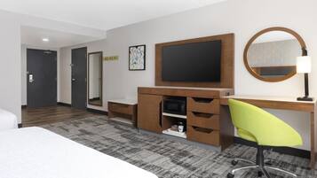Habitación de hotel con cama, escritorio, silla, televisor, microondas y espejo.