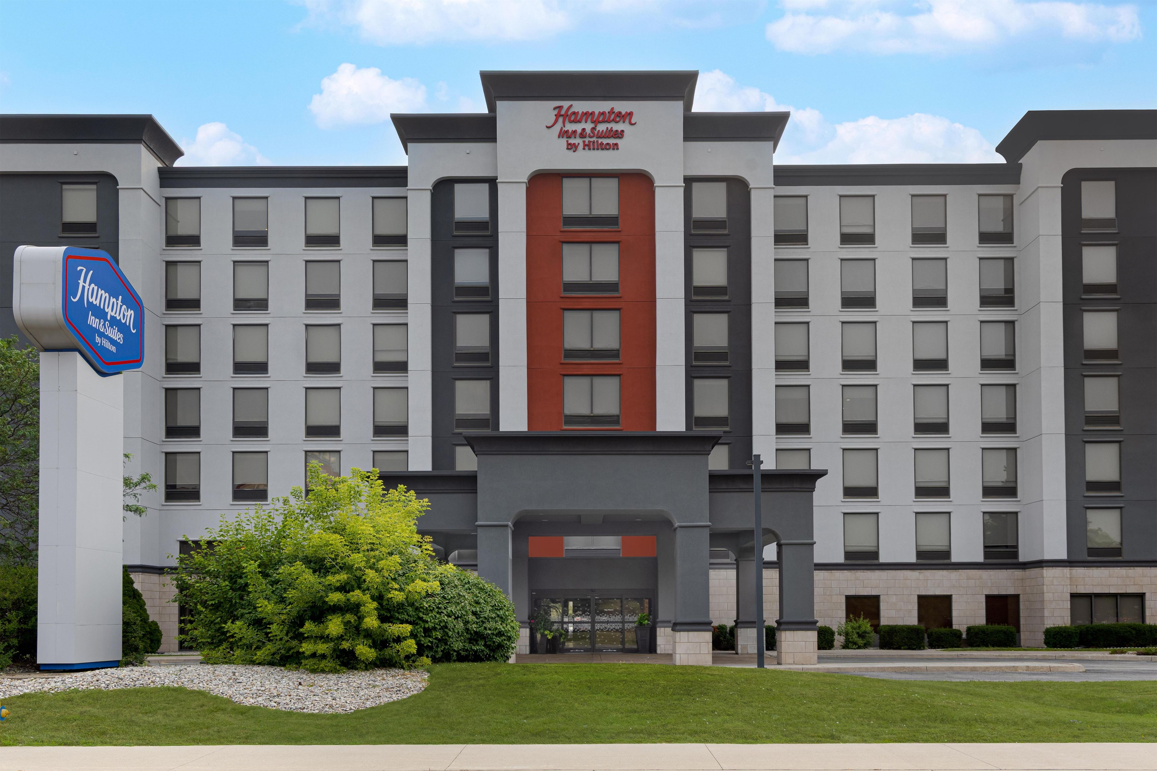 A Hampton Inn & Suites hotel with a modern facade, multiple windows, and a prominent entrance.