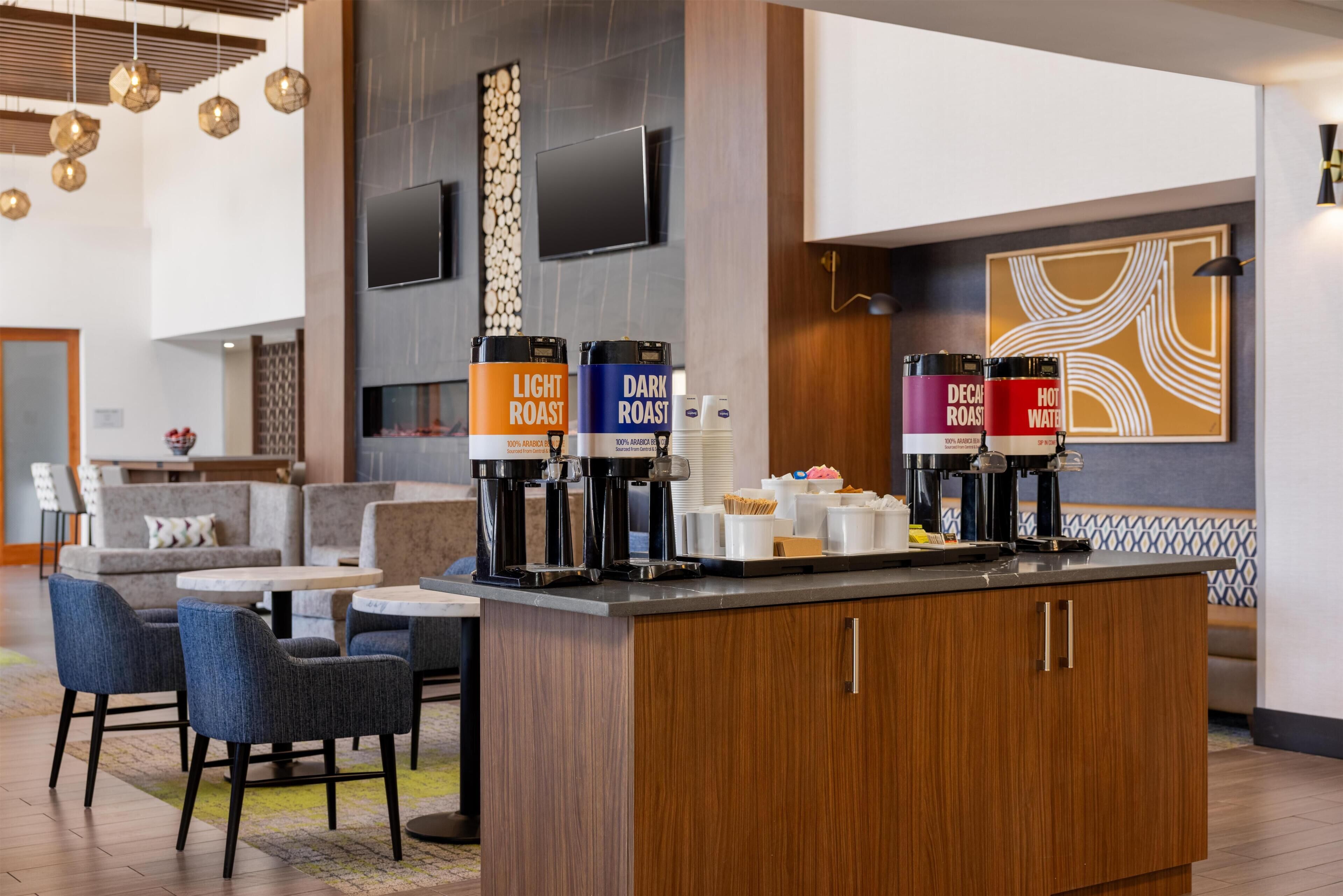 Un hall d’hôtel moderne doté d’un espace café, d’un coin salon et d’un téléviseur à écran plat fixé au mur.