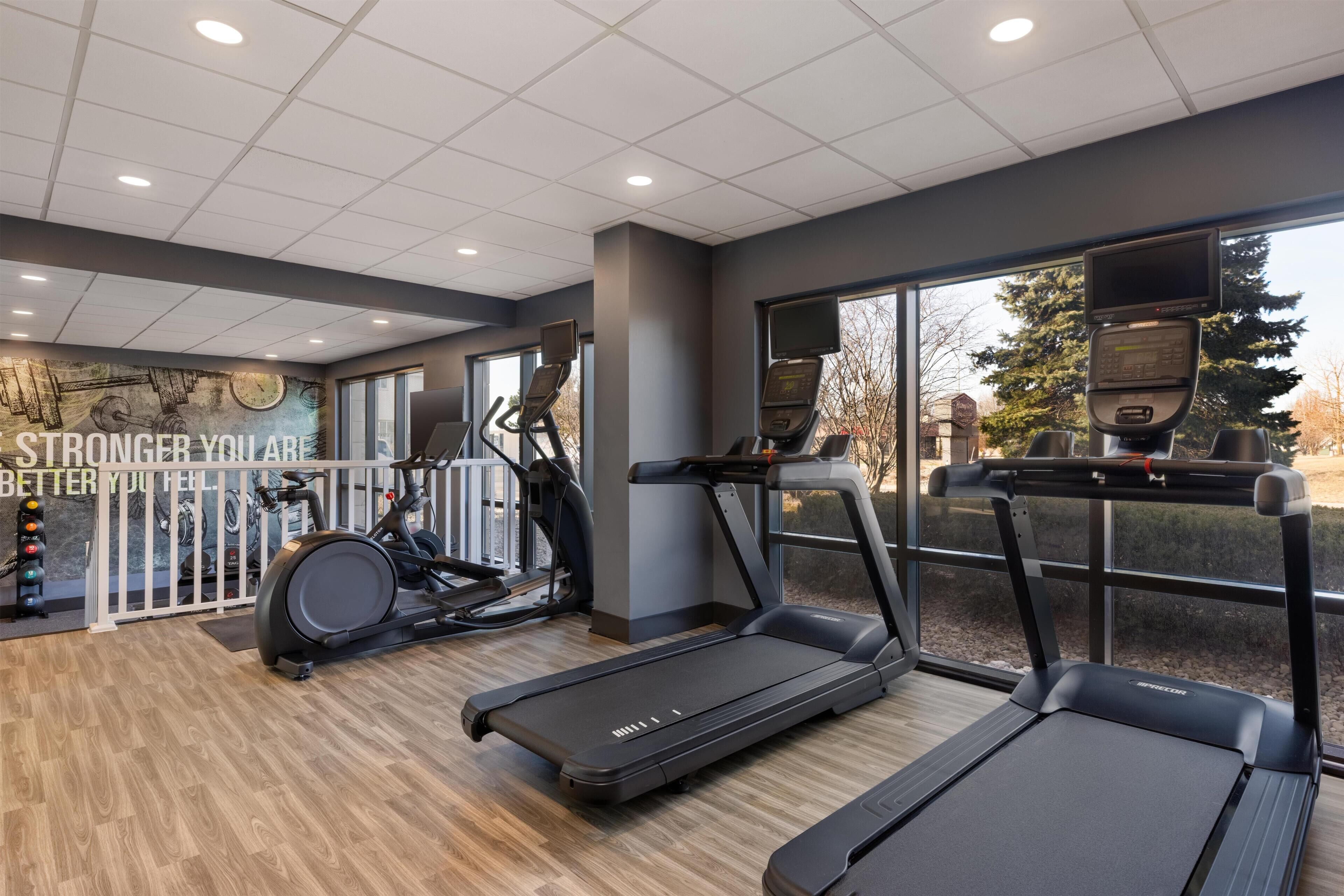 Une salle de sport équipée de tapis de course, de vélos d’appartement et d’un mur orné de messages motivants.